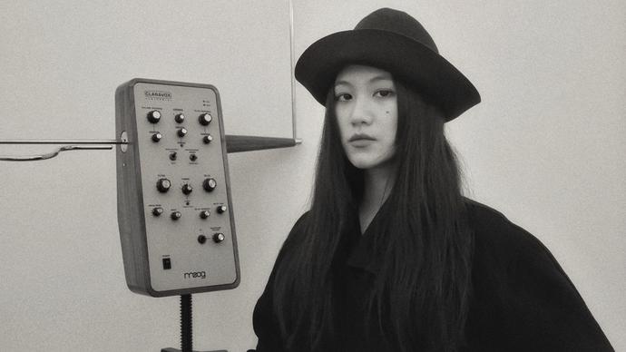 Li Yilei is dressed in a black shirt and hat, standing to the right of their theramin. The image is black and white.