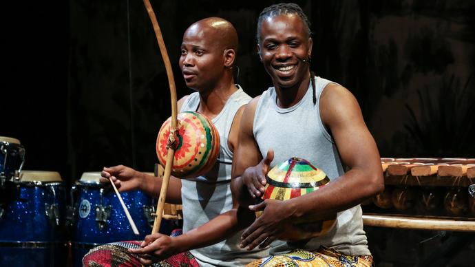 Two performers smile as they make music using instruments together.