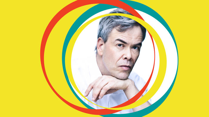 Hannu Lintu leans on his hand. Yellow BBC SO branding surrounds his centralised image