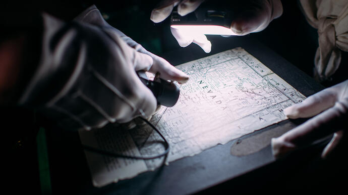 Three hands shine lights on a map that says 'Sevada' on it.