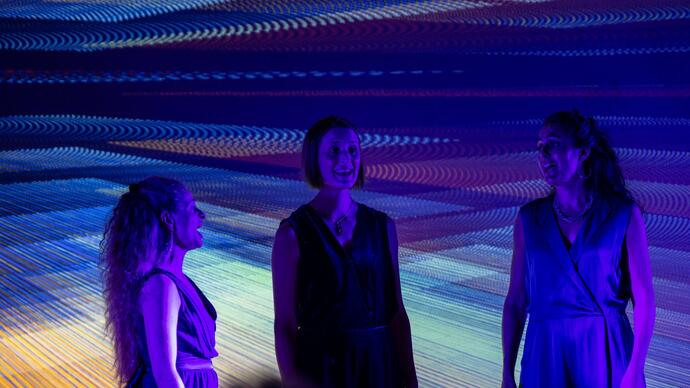 The three members of Voice Trio singing on stage, with purple lights and a purple projection behind them