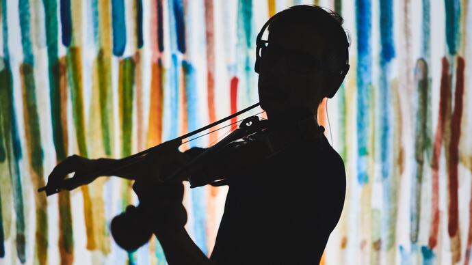 A silhouette of a violinist in front of a multi colour background