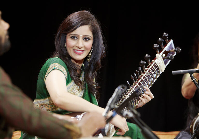 Roopa Panesar on stage playing an instrument smiling