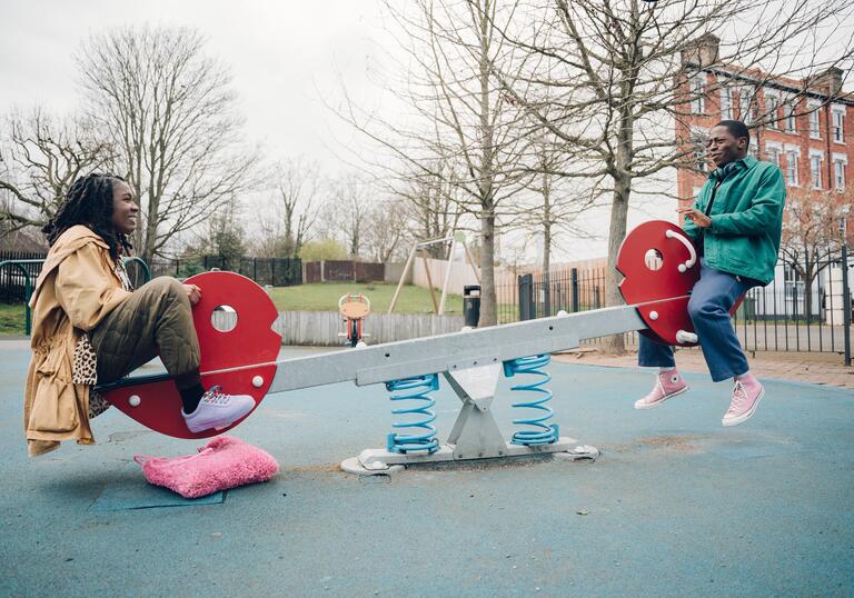 A man and woman sit on a seesaw