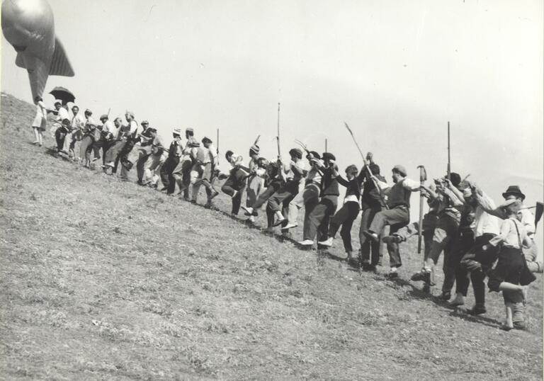 Locals run up a hill to catch up to a barrage balloon