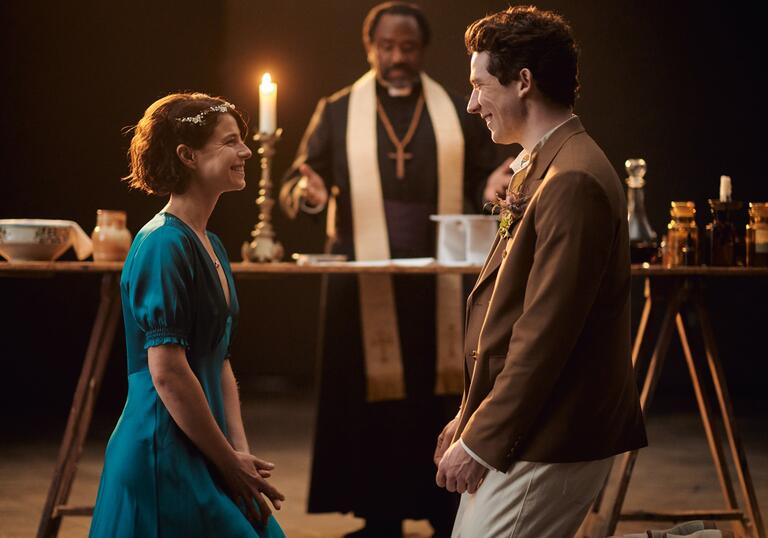 Romeo and Juliet marry, smiling hugely at each other in front of Friar Lawrence, in a candlelit hall.