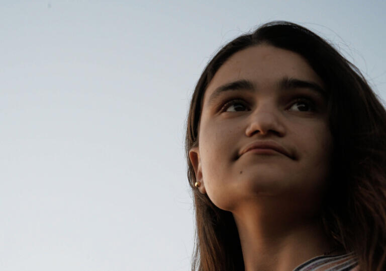 A woman looks into the distance against a sunset
