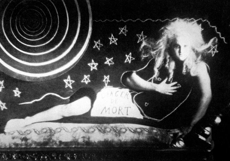 A man with large hair reclines on a chaise lounge with drawn stars and a sun behind him.