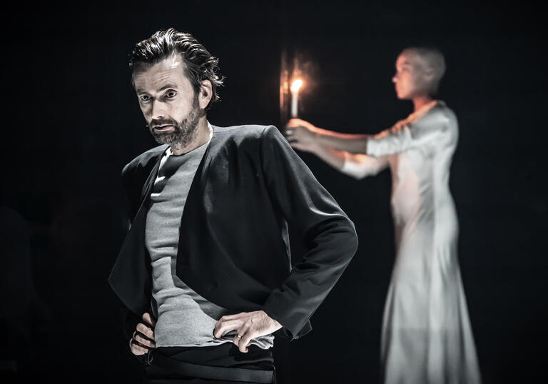A man stands with his back to a woman on a dark stage.