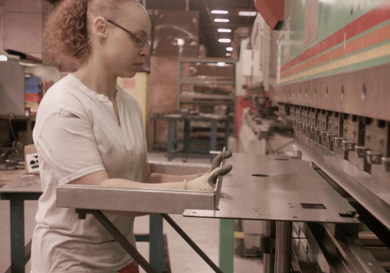 A worker holds a piece of metal against a machine.