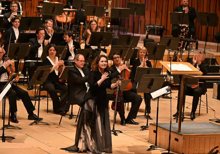 Patricia Kopatchinskaja on stage at the Barbican Hall with her hand on her chest smiling