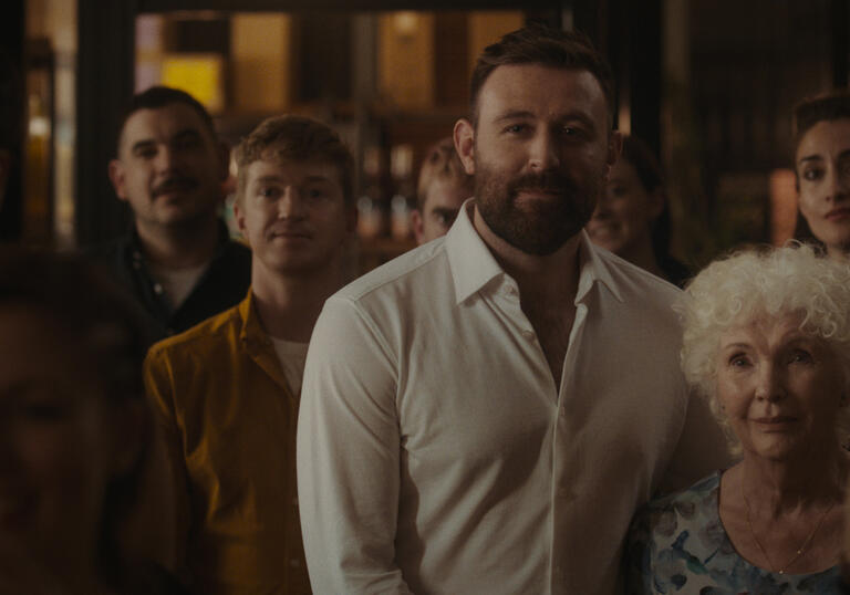 A middle aged man and his elderly mother smile in a crowd.