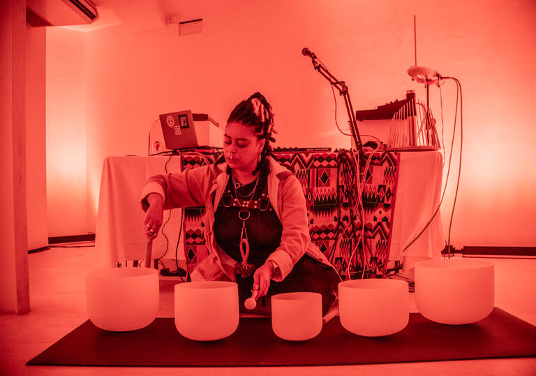 Hannah Catherine Jones sits in a room lit by an orange light playing bowl-shaped objects.