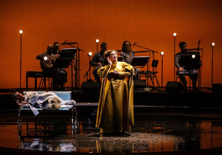 A photo of a singer on stage, with an orchestral ensemble in the background. Semi staged production of Bushra El-Turk's Oum - A Son's Quest for his Mother