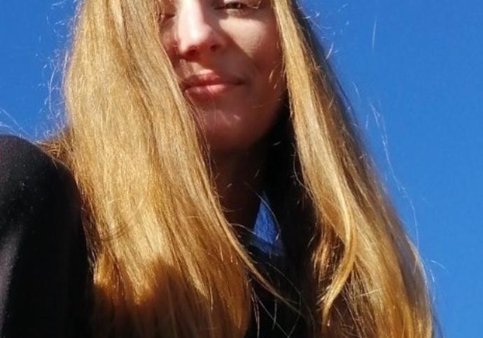 girl with blonde hair wearing black jumper standing outside in the sun.