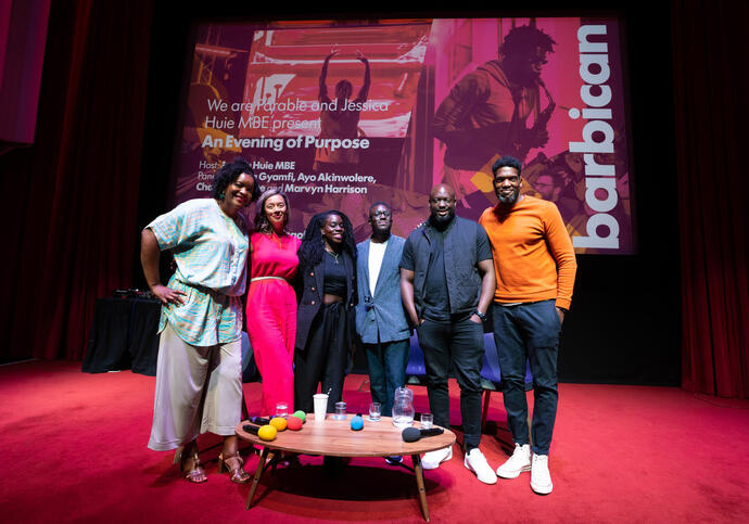 Six people standing around on stage with background of 'An Evening of Purpose'