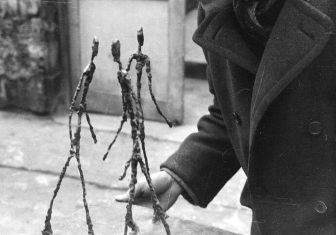 A black and white photo of Alberto Giacometti in his studio holding his sculpture, Three Men Walking.