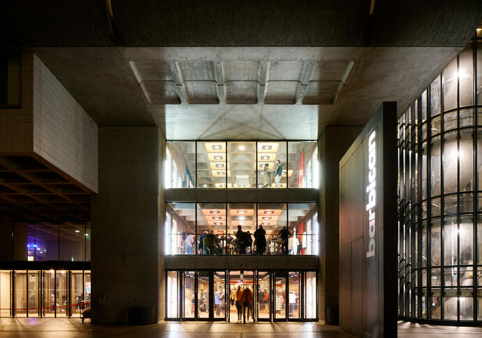 A night time shot of the Barbican looking inside to bright light and people