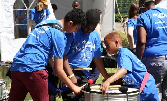 three people playing a metal drum