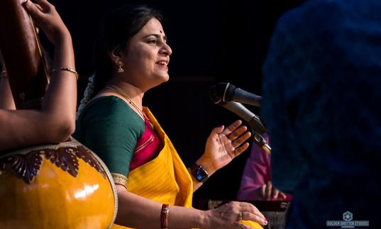 Bharathi Prathap singing, sitting cross-legged and wearing colourful clothes
