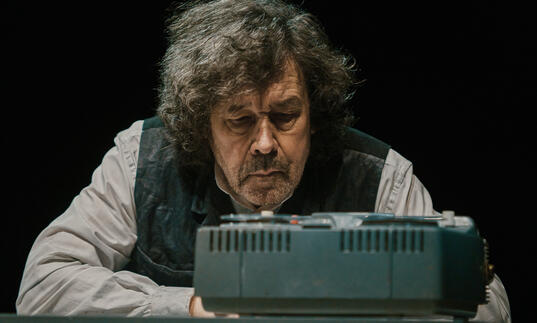 Actor Stephen Rea sits in front of a tape machine.