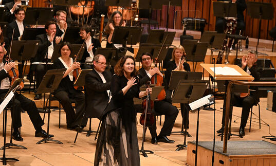 Patricia Kopatchinskaja on stage at the Barbican Hall with her hand on her chest smiling