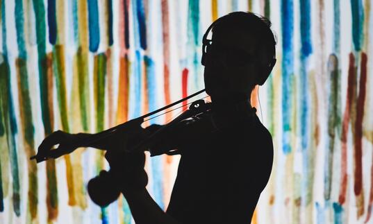 A silhouette of a violinist in front of a multi colour background