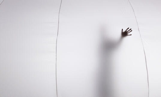 The silhouette of a person can be seen from inside a bubble, their hand is pressed against the material.